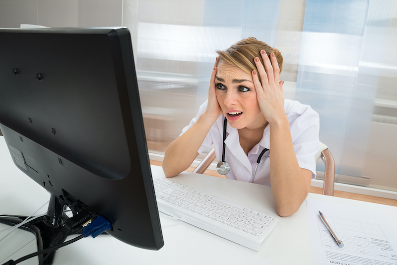 Worried Doctor Looking At Computer In Clinic