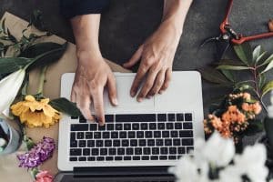 Hands on a laptop, with flowers to the side